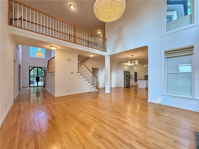 6765 Crofton Dr, Alpharetta, GA 30005 - unfurnished living room featuring a chandelier, a high ceiling, light wood-style floors, stairway, and baseboards