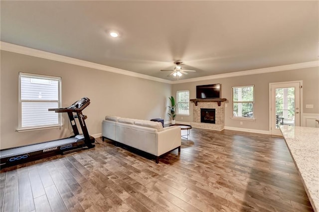 living area with a ceiling fan, a fireplace with raised hearth, wood finished floors, and crown molding