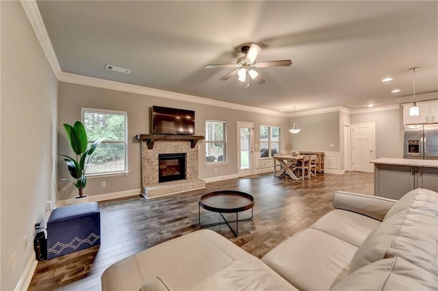 living area with dark wood-style flooring, ceiling fan, ornamental molding, a glass covered fireplace, and baseboards