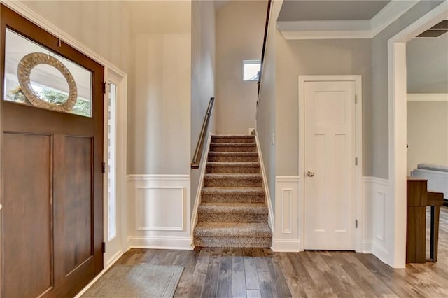 foyer with wood finished floors, a wainscoted wall, stairway, a decorative wall, and crown molding