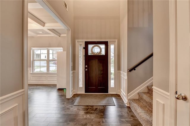 entrance foyer featuring a decorative wall, coffered ceiling, dark wood-style flooring, beam ceiling, and stairway