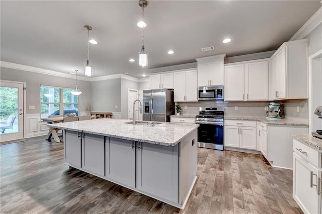 kitchen with appliances with stainless steel finishes, a sink, crown molding, a kitchen island with sink, and wood finished floors