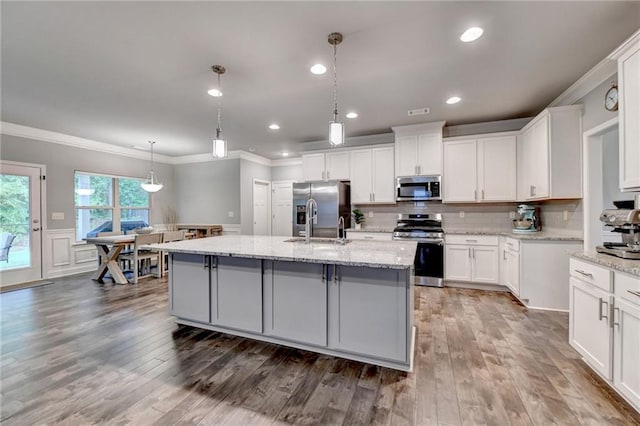 kitchen featuring appliances with stainless steel finishes, ornamental molding, an island with sink, a sink, and white cabinets