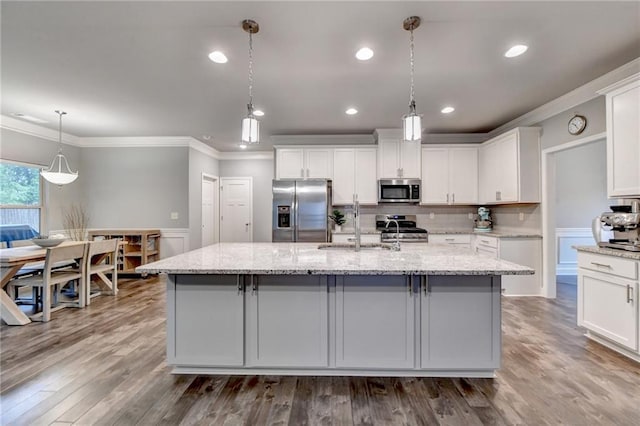 kitchen featuring stainless steel appliances, ornamental molding, a sink, a center island with sink, and white cabinets
