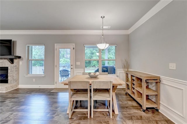 dining area featuring crown molding, hardwood / wood-style floors, a wainscoted wall, a stone fireplace, and a decorative wall