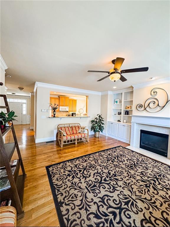 living room with crown molding, light wood finished floors, a fireplace with flush hearth, a ceiling fan, and baseboards