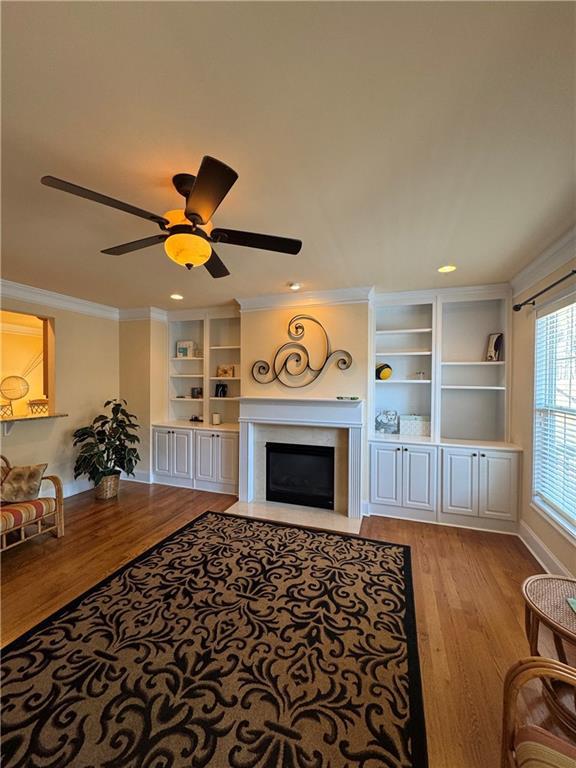 living area with ornamental molding, a fireplace with flush hearth, ceiling fan, and light wood finished floors