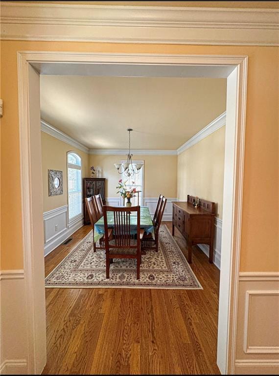 dining area featuring a wainscoted wall, wood finished floors, visible vents, ornamental molding, and an inviting chandelier