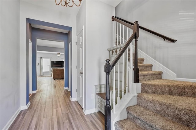 stairway with an inviting chandelier, baseboards, and wood finished floors