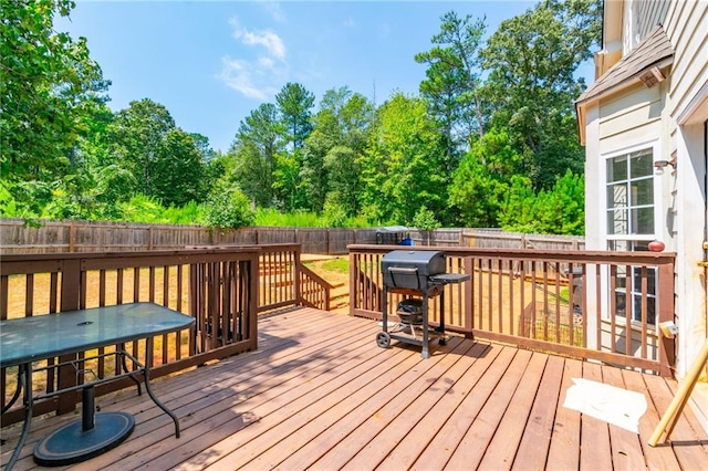 deck with a fenced backyard, outdoor dining area, a grill, and view of wooded area