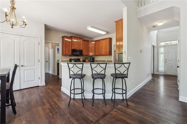 kitchen featuring black microwave, dark wood-type flooring, a kitchen breakfast bar, a chandelier, and brown cabinets