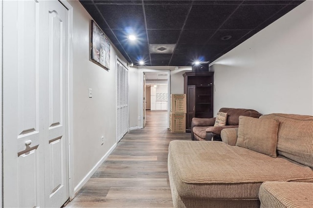 living area with wood finished floors, a drop ceiling, and baseboards