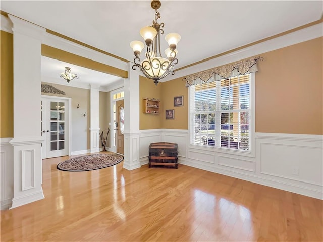 entryway featuring a wainscoted wall, an inviting chandelier, ornamental molding, wood finished floors, and ornate columns