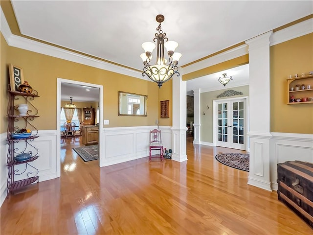 dining space featuring french doors, a notable chandelier, decorative columns, and light wood finished floors