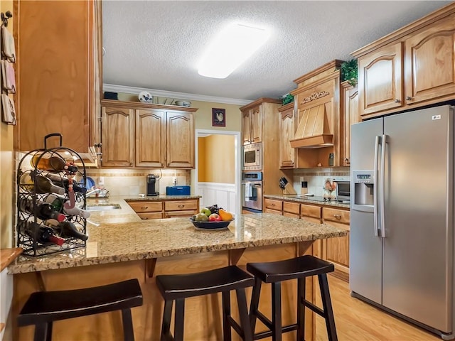 kitchen with light wood finished floors, light stone counters, a breakfast bar, a peninsula, and stainless steel appliances