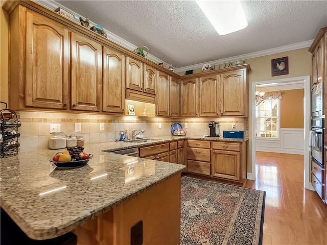 kitchen featuring a peninsula, stainless steel appliances, a sink, ornamental molding, and light wood finished floors