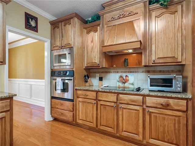 kitchen featuring light stone counters, premium range hood, light wood-style floors, appliances with stainless steel finishes, and crown molding