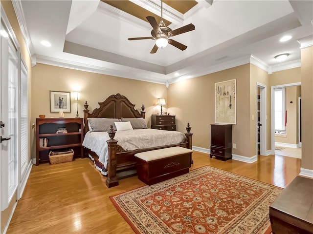 bedroom featuring light wood finished floors, baseboards, a tray ceiling, and ornamental molding