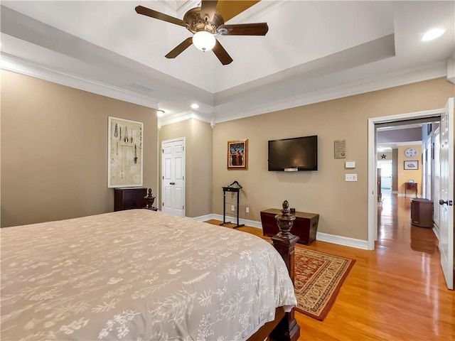 bedroom with ornamental molding, a tray ceiling, light wood-style flooring, and baseboards