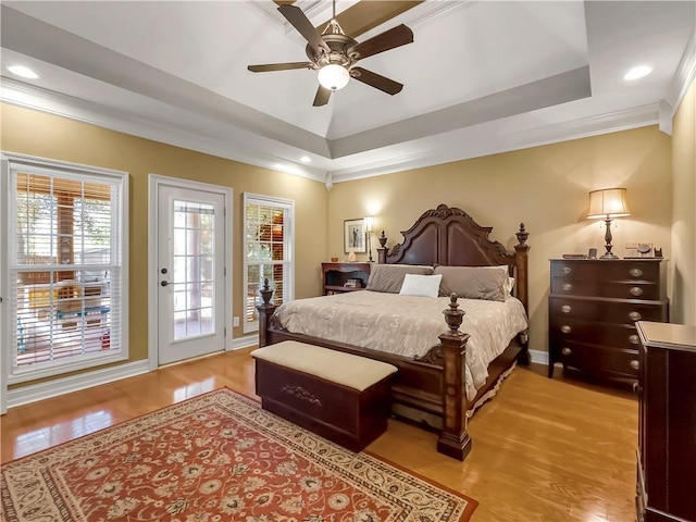 bedroom featuring crown molding, light wood-style floors, a raised ceiling, and access to exterior