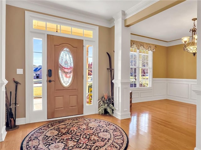 foyer featuring ornate columns, light wood-style flooring, crown molding, and an inviting chandelier