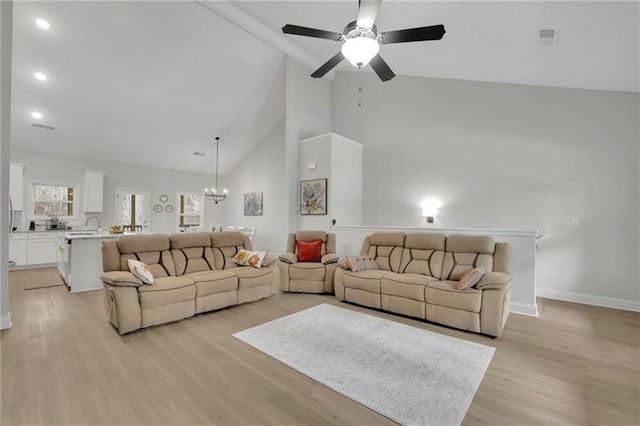 living room with ceiling fan with notable chandelier, high vaulted ceiling, and light hardwood / wood-style floors