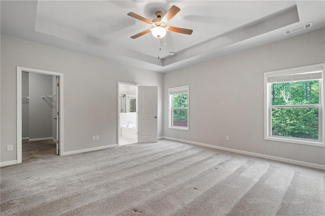unfurnished bedroom featuring carpet flooring, a raised ceiling, baseboards, a spacious closet, and visible vents