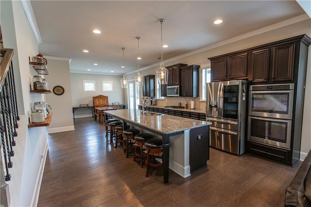 6390 Yellow Birch St, Cumming, GA 30040 - kitchen featuring appliances with stainless steel finishes, dark brown cabinetry, a kitchen breakfast bar, light stone counters, and a center island with sink