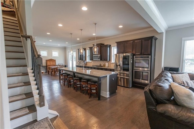 6390 Yellow Birch St, Cumming, GA 30040 - kitchen featuring appliances with stainless steel finishes, open floor plan, dark brown cabinets, a breakfast bar area, and dark wood-type flooring