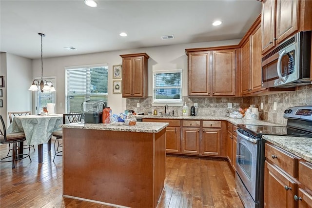 kitchen featuring stainless steel appliances, a center island, visible vents, light stone countertops, and dark wood-style floors