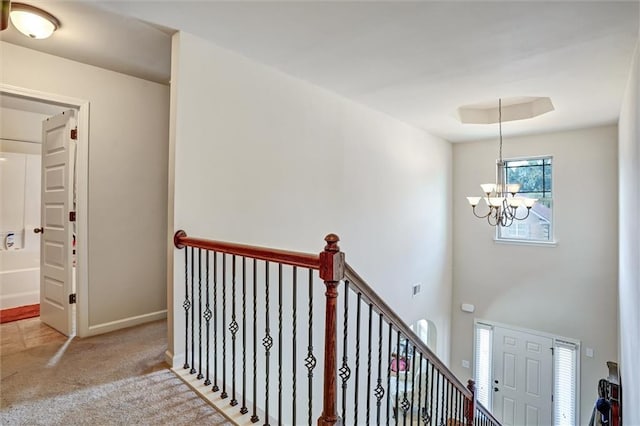 hall featuring baseboards, carpet, a tray ceiling, an upstairs landing, and a chandelier