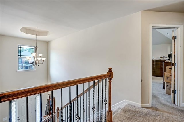 hall featuring a notable chandelier, a raised ceiling, light carpet, an upstairs landing, and baseboards