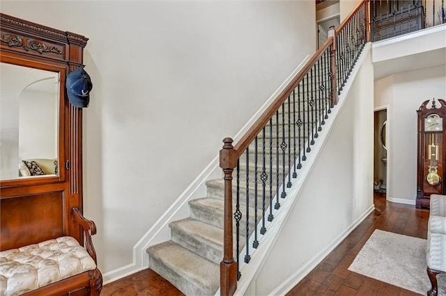 stairway with a towering ceiling, baseboards, and hardwood / wood-style floors