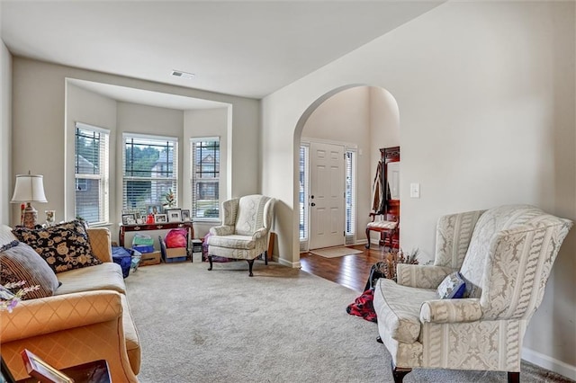 living room with baseboards, visible vents, arched walkways, and carpet flooring