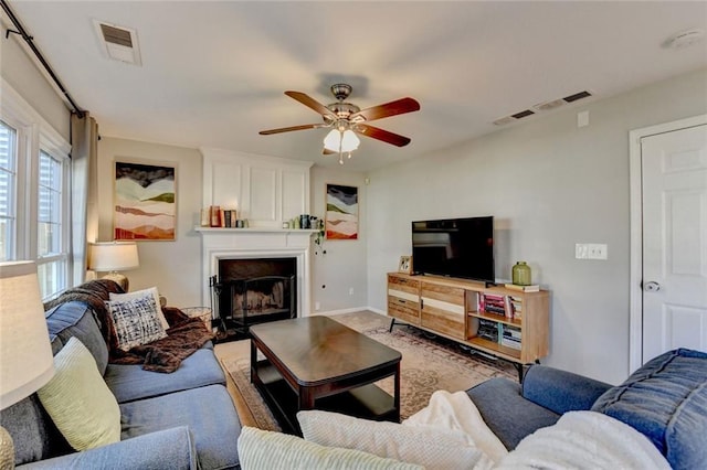 living room with a large fireplace, ceiling fan, and visible vents