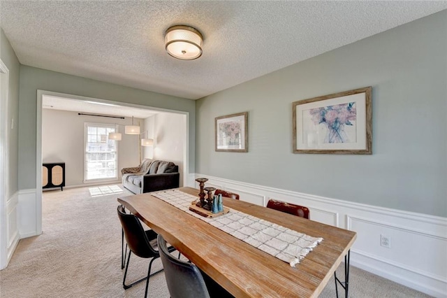 dining area with wainscoting, a textured ceiling, and light colored carpet