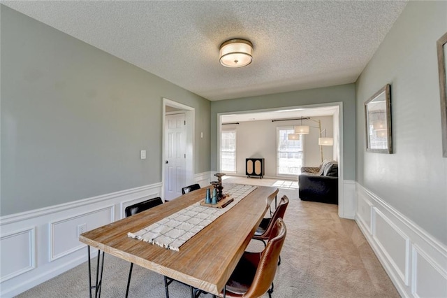 dining room with light carpet, a wainscoted wall, a decorative wall, and a textured ceiling