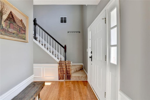 entryway with light wood-type flooring, wainscoting, a decorative wall, and stairs