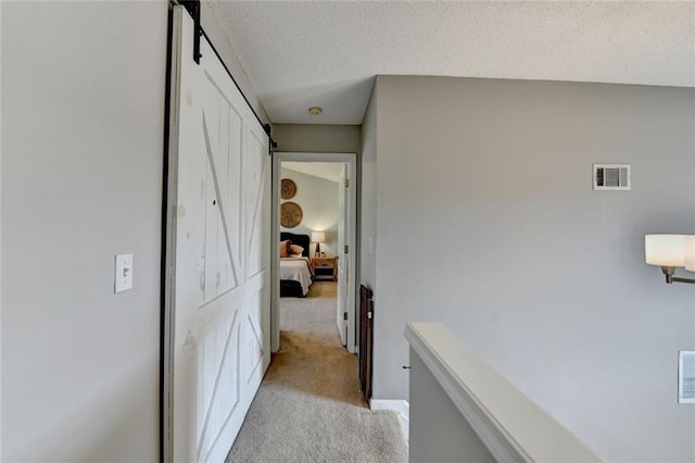 hallway featuring visible vents, light carpet, a textured ceiling, and a barn door