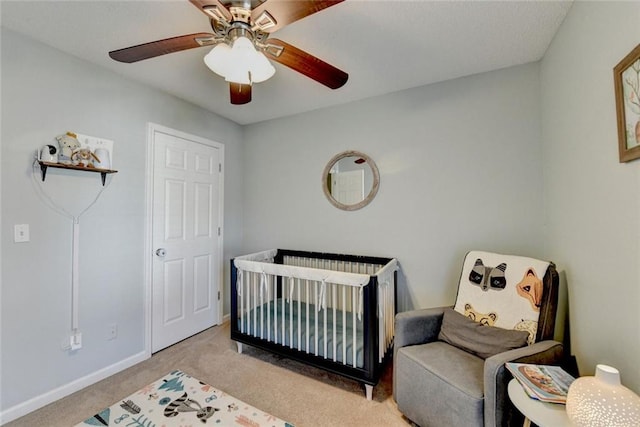 bedroom featuring light carpet, ceiling fan, a crib, and baseboards