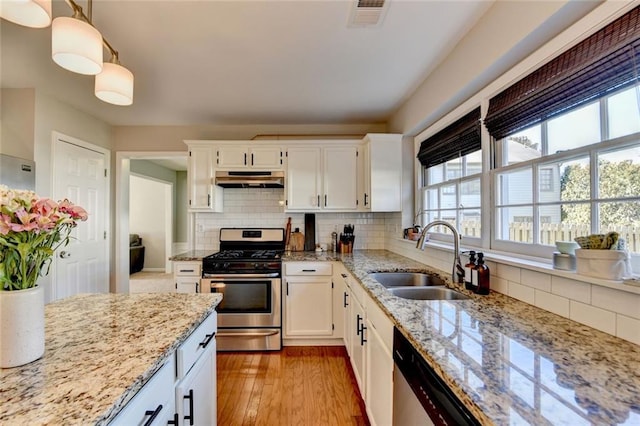 kitchen featuring light wood-style flooring, under cabinet range hood, stainless steel appliances, a sink, and visible vents