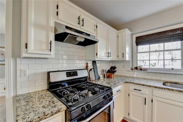 kitchen featuring light stone counters, under cabinet range hood, white cabinets, backsplash, and gas stove