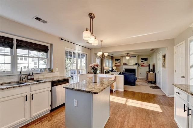 kitchen featuring light wood finished floors, a center island, stainless steel dishwasher, a fireplace, and a sink