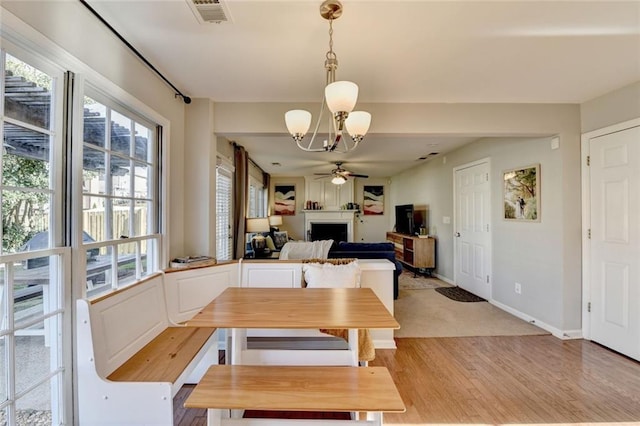 dining room with ceiling fan with notable chandelier, a fireplace, visible vents, baseboards, and light wood-type flooring