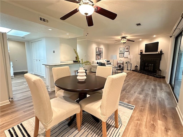 dining area with a skylight, light hardwood / wood-style flooring, ornamental molding, and ceiling fan