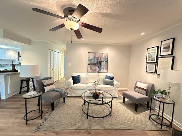 living area featuring a textured ceiling, recessed lighting, wood finished floors, baseboards, and crown molding