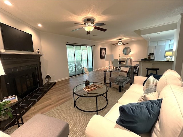 living room featuring a textured ceiling, recessed lighting, wood finished floors, baseboards, and a tiled fireplace