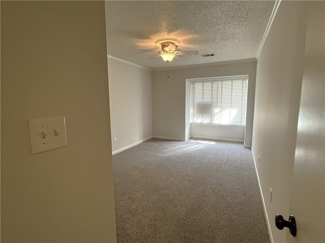 carpeted spare room featuring a ceiling fan, visible vents, a textured ceiling, and ornamental molding