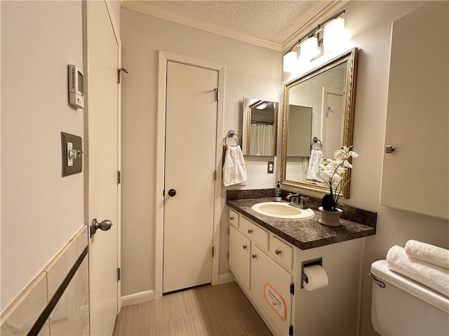 bathroom with toilet, ornamental molding, wood finished floors, a textured ceiling, and vanity