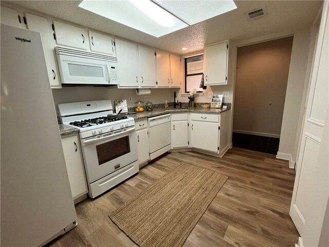 kitchen featuring light wood-type flooring, kitchen peninsula, white appliances, dark stone counters, and white cabinets